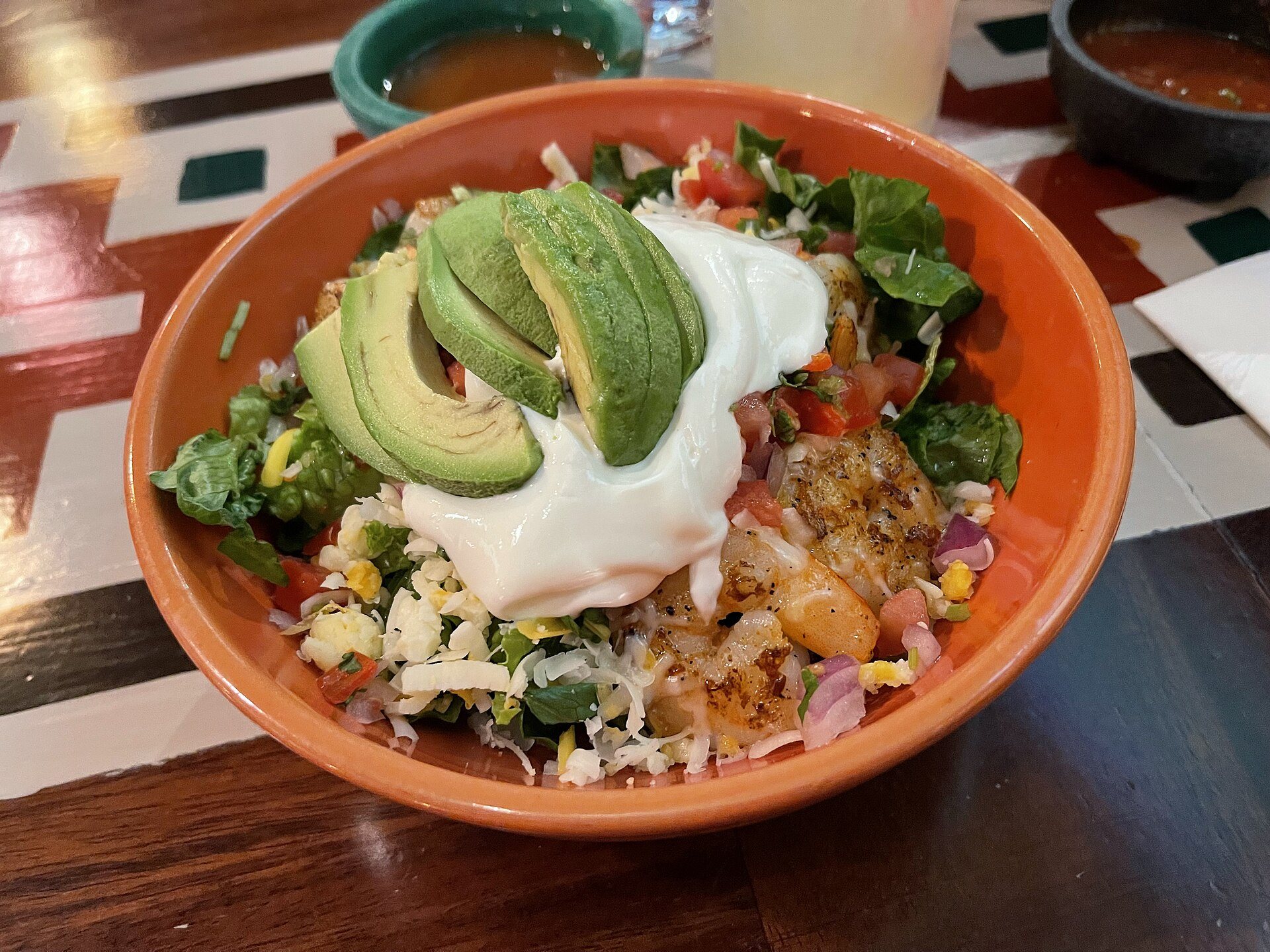 Burrito bowl with rice, black beans, avocado slices, sour cream and salsa in an orange bowl