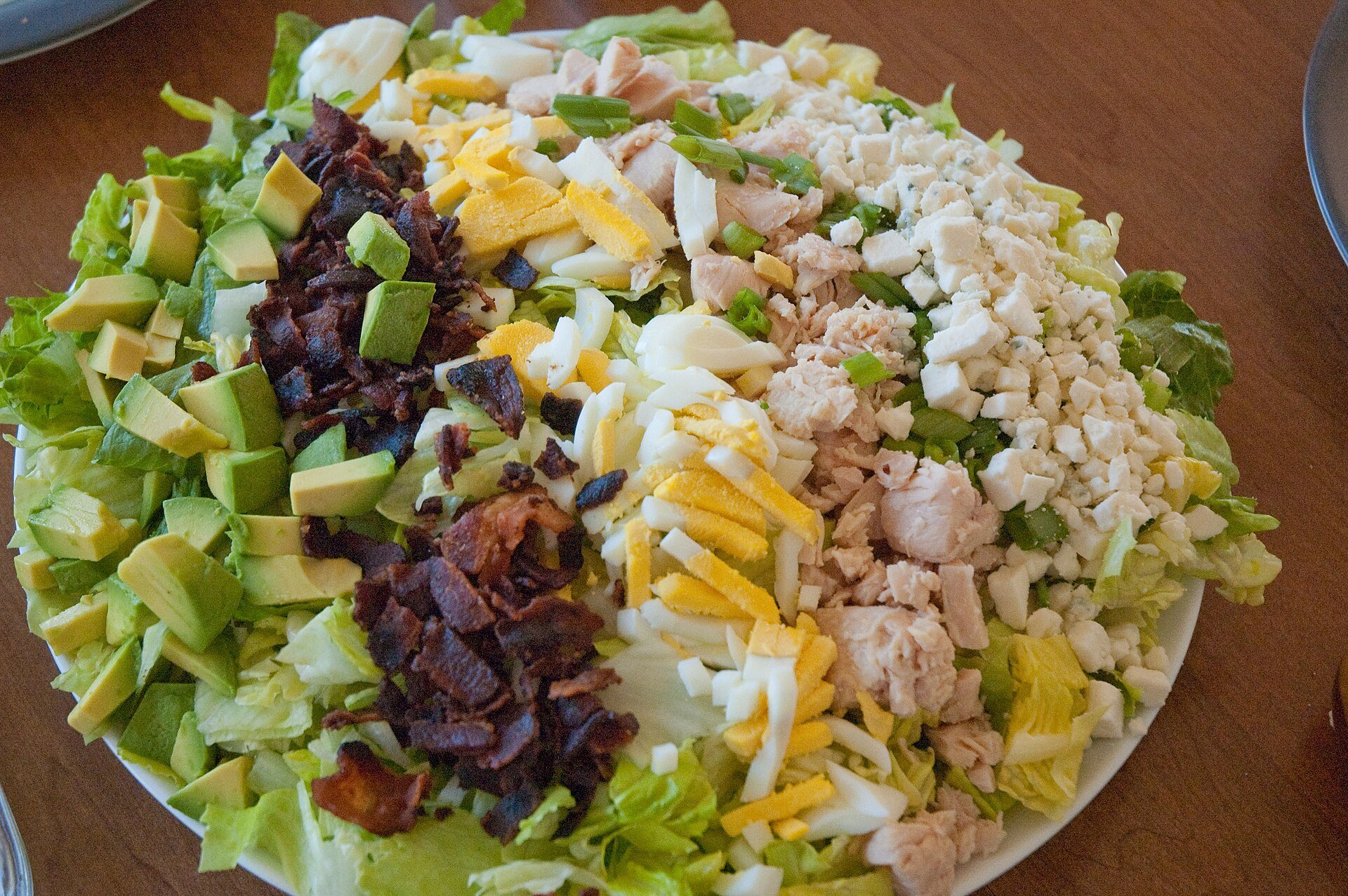 Cobb salad with rows of chicken, bacon, egg, avocado, blue cheese and tomato on lettuce