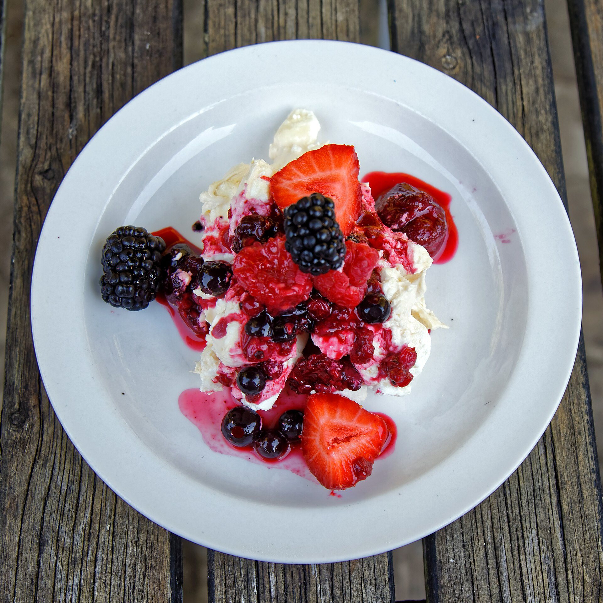 Eton mess with crushed meringue, cream, strawberries and blackberries on a white plate
