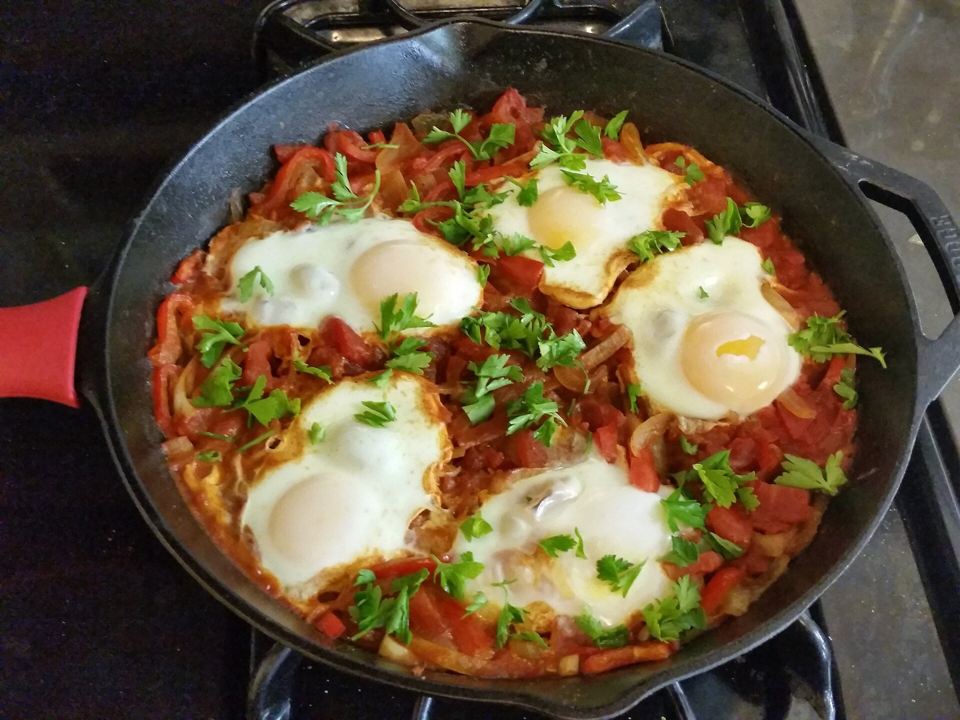 Shakshuka with eggs in tomato sauce, topped with chopped parsley, in a cast-iron skillet on the stove