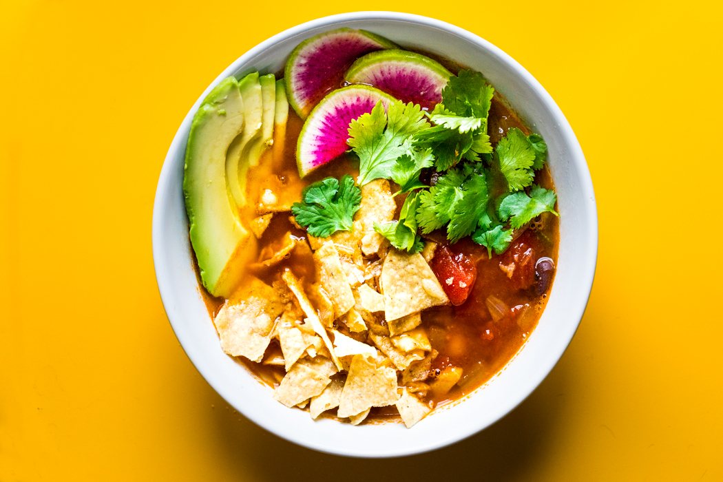 Tortilla soup topped with avocado, radish, cilantro and crispy tortilla strips